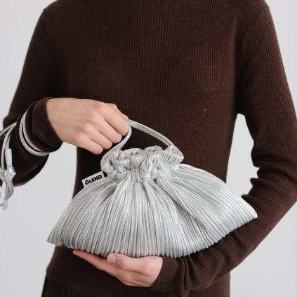 Shell Bag je vyrobena z jemně plisované tkaniny, kterou lze nosit staženou pro výrazný, sochařsky působící vzhled, nebo volně pro ležérnější siluetu. Po stažení připomíná tvar mořské mušle, která se stala inspirací pro její název. Je ideální na speciální příležitosti, ale snadno ji zkombinujete i s každodenním outfitem.  • Lehká a elegantní konstrukce • Jemně plisovaný materiál • Hlavní prostor se stahovacím uzavíráním • Vnitřní kapsa na drobnosti • Dva crossbody popruhy • Vodoodpudivý nylonový materiál • Ideální na slavnostní události i běžné nošení • Dodávána v ekologickém balení  Rozměry: 35 × 20 cm  Materiál: vodoodpudivý nylon  Péče: Tašku čistěte jemným kartáčkem, vlažnou vodou a mýdlem.